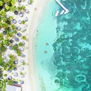 Luxury resort with swimming pool and beach umbrellas on palm fringed beach from above, Antigua, Caribbean, West Indies