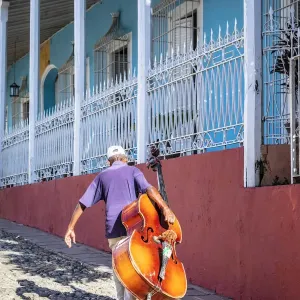 A man carrying a cello in Plaza Mayor in Trinidad, Sancti Spiritus, Cuba A man carrying a cello in Plaza Mayor in Trinidad, Sancti Spiritus, Cuba