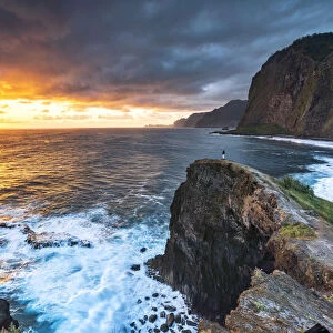 Man on cliffs looking at waves at dawn, Miradouro Do Guindaste viewpoint, Madeira island