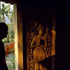 Monk standing by the door of Wat Mai Suwannaphumaham