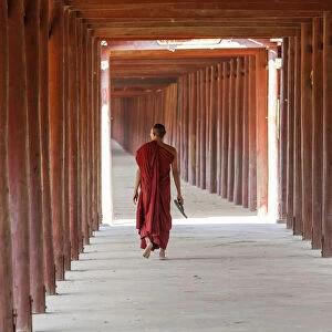 Monk in walkway of wooden pillars to temple, Salay, Myanmar, (Burma)