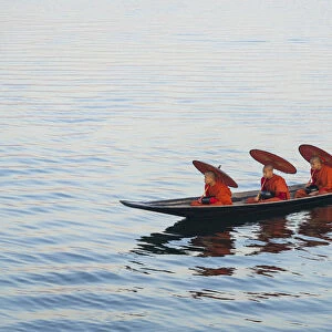 Three monks in orange robes with bowls for alms giving and a leg-rowing fisherman commute