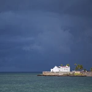 Mozambique, Ihla de Mozambique, Stone Town. The Church of Santo Antonio stands illuminated ahead of a dark approaching storm