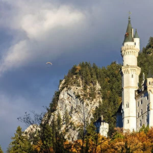 Neuschwanstein Castle framed by paraglide in the cloudy sky and the colorful woods