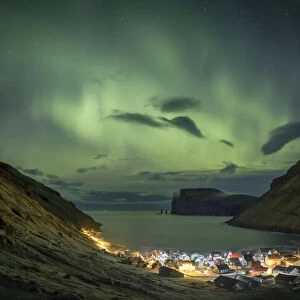 Northern lights above the village of TjornuvÔêÜÔëák. In the background Risin and Kellingin sea stacks. Streymoy island, Faroe Islands