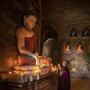 A novice monk holding a burning candle while praying by Buddha statue, UNESCO, Bagan