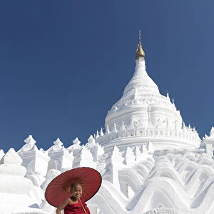 Novice monk sits on the white wall of Hsinbyume Pagoda holding a red umbrella, Mingun
