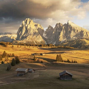 Some old cabins lost in the meadows of the Alpe di Siusi (Seiser Alm) during an early autumn sunset, with the Sassolungo and Sassopiatto in the background. Dolomites, Italy