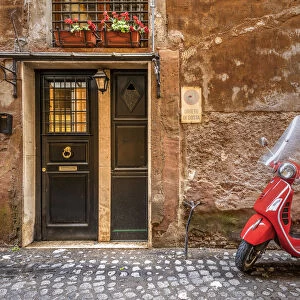 Parked red Vespa scooter in a cobbled street of Rome, Lazio, Italy