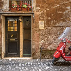 Parked red Vespa scooter in a cobbled street of Rome, Lazio, Italy