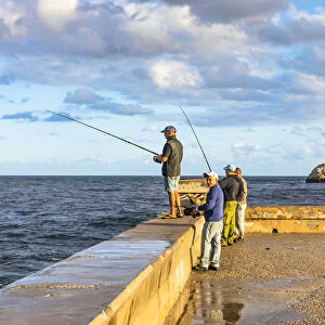 People fishing early in the morning on the Malecon, with Castillo De Los Tres Reyes Del