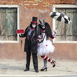 Two people pose in front of a colourful facade on Burano during the Venice Carnival
