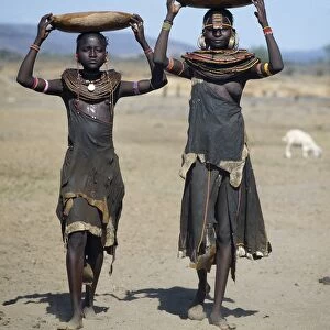 Two Pokot girls carry water in wooden containers on their heads