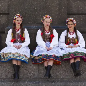 Poland, Cracow. Polish girls in traditional dress sitting at the base of the statue of Adam Mickiewicz, preparing to dance in