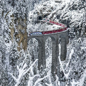 Red train Travelling on the Landawasser Viadukt through the vegetation covered in snow