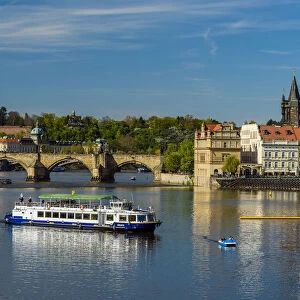 River cruise boat on Vltava River with Smetana Museum and Charles Bridge in the background