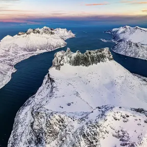Romantic sunrise over the snowy peak of Grytetippen mountain along the icy sea, aerial view, Ornfjord, Senja, Troms, Norway Romantic sunrise over the snowy peak of Grytetippen mountain along the icy sea, aerial view, Ornfjord, Senja, Troms, Norway