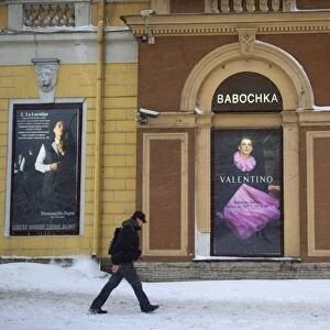 Russia, St. Petersburg; A man walking in front of high end clothes adverts in the city centre in Winter