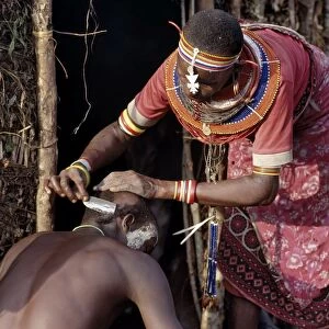 A Samburu mother shaves her sons head outside