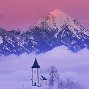 Slovenia, Jamnik, Church of St. Primoz sorrounded by fog at dusk with the Kamnik-Savinja Alps beyond, Gorenjska