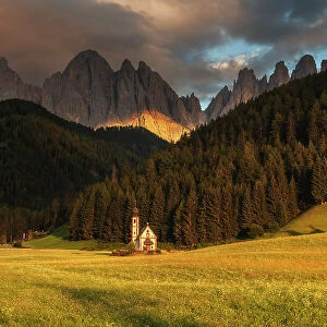 The small chapel of San Giovanni in Ranui taking the last light of the day with the imposing Odle mountains in the background. Dolomites, Italy