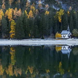 The small chapel on the shores of the Braies lake (Pragser Wildsee) with larches and firs reflecting in the lake. Dolomites, Italy