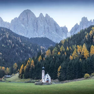 The small chapel of St. Johann in Ranui at twilight during a gloomy autumn evening, with the Odle mountains in the background. Dolomites, Italy