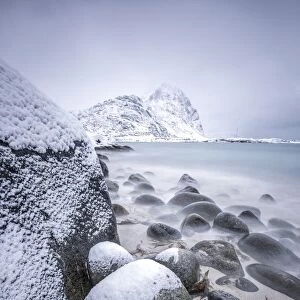 Snow covered rocks on the beach modeled by the wind surround the icy sea Pollen Vareid