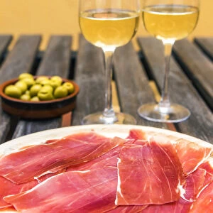Spanish ham or jamon iberico served with glasses of white wine and olives in a tapas bar