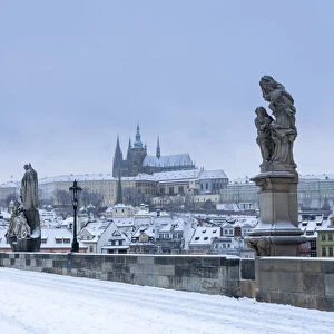 Statues at snow-covered Charles bridge and Prague Castle in winter, Prague, Bohemia