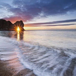 Sun shining through Durdle Door at sunrise, Jurassic Coast, Dorset, England, UK