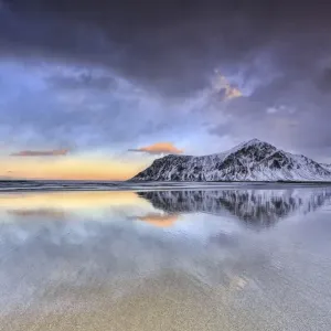 Sunset on Skagsanden beach surrounded by snow covered mountains reflected in the cold sea Sunset on Skagsanden beach surrounded by snow covered mountains reflected in the cold sea
