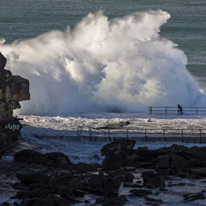 Swimmer braces as waves crash over rocks at North Curl Curl rockpool, New South Wales