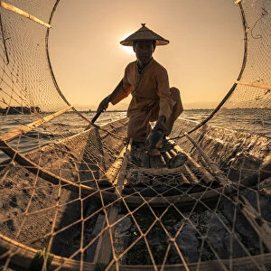 Traditional fisherman viewed through conical fishing net collecting fish on a boat