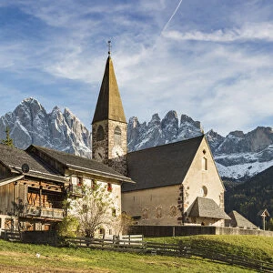 Typical houses and the church of the village with Odle Dolomites peaks on the background