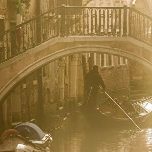 Venice, Veneto, Italy. Gondolier on a Gondola passing under a bridge, backlight view