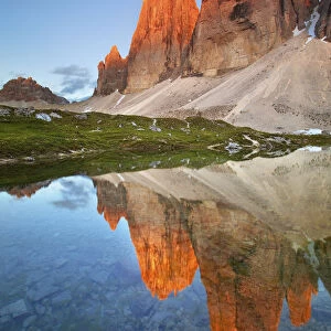 A waterhole its reflecting the Lavaredos Three Peaks, illuminated by the