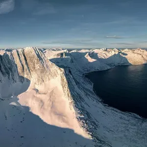 Winter sunrise over Breidtinden mountain covered with snow overlooking the cold sea, Mefjorden, Senja, Troms county, Norway Winter sunrise over Breidtinden mountain covered with snow overlooking the cold sea, Mefjorden, Senja, Troms county, Norway