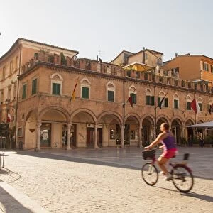 Woman cycling through Piazza del Popolo, Ascoli Piceno, Le Marche, Italy