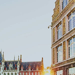 A woman riding a bike in Bruges Market Square at sunrise, Belgium
