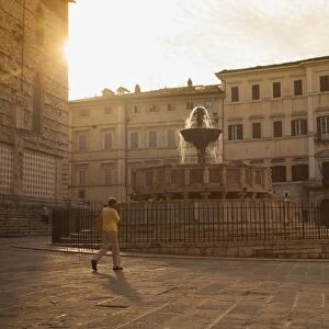 Woman walking past Fontana Maggiore in Piazza IV Novembre at dawn Perugia, Umbria, Italy