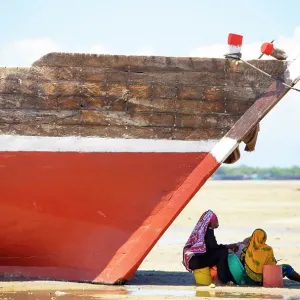 Two women sitting in the shade of a fishing boat on the beach, Mkokotoni, Zanzibar, Tanzania Two women sitting in the shade of a fishing boat on the beach, Mkokotoni, Zanzibar, Tanzania