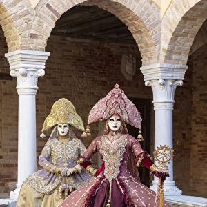 Two women wearing Indian style costumes and masks pose in the cloisters of Chiesa di San