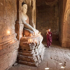 Young Buddhist monk prays in front of a statue of Buddha in a temple in Bagan, Myanmar
