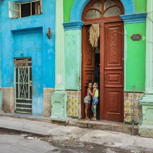 Two young girls peaking through the door of their house in Centro Habana Province, Havana