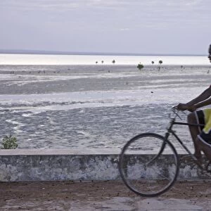 A young man cycling along the sea wall on Ibo Island