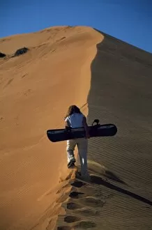 Adventurer Gallery: An adventurer climbs a sand dune with a sand board