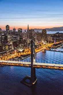 Suspension Bridge Collection: Aerial of downtown district at dusk with Bay bridge in the foreground, San Francisco