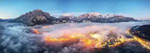Highway Prints: Aerial panoramic of the illuminated town of Lecco and mountains under the foggy sky at dusk
