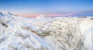 Aerial panoramic of Stelvio Pass and winding road covered with snow at dawn, Bormio